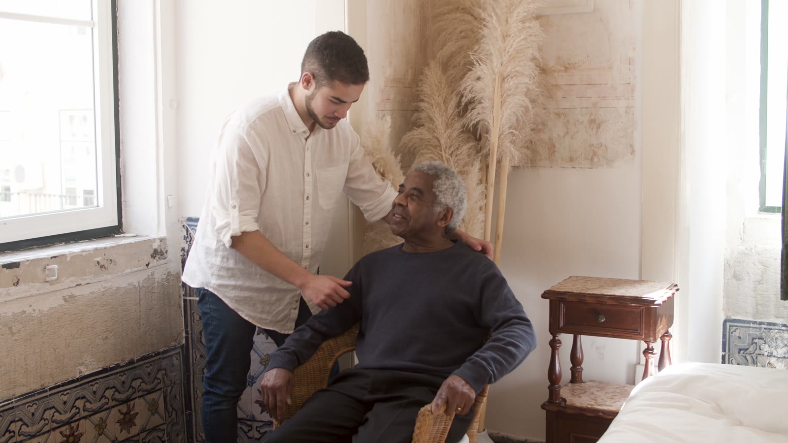A caregiver checks in with an older man in a bright, calm room.