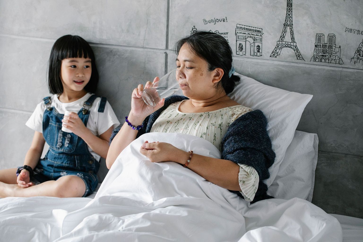 A mother and daughter share a drink of water at home.