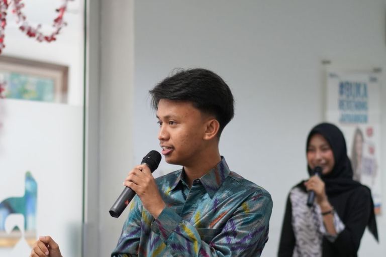 A young man speaks into a microphone while a colleague listens.