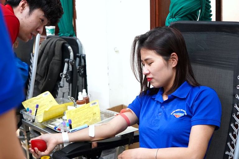 A young woman gives blood while a health worker assists.